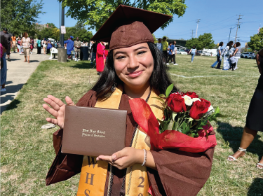 female student wearing cap and gown holding high school diploma in hands smiling for camera